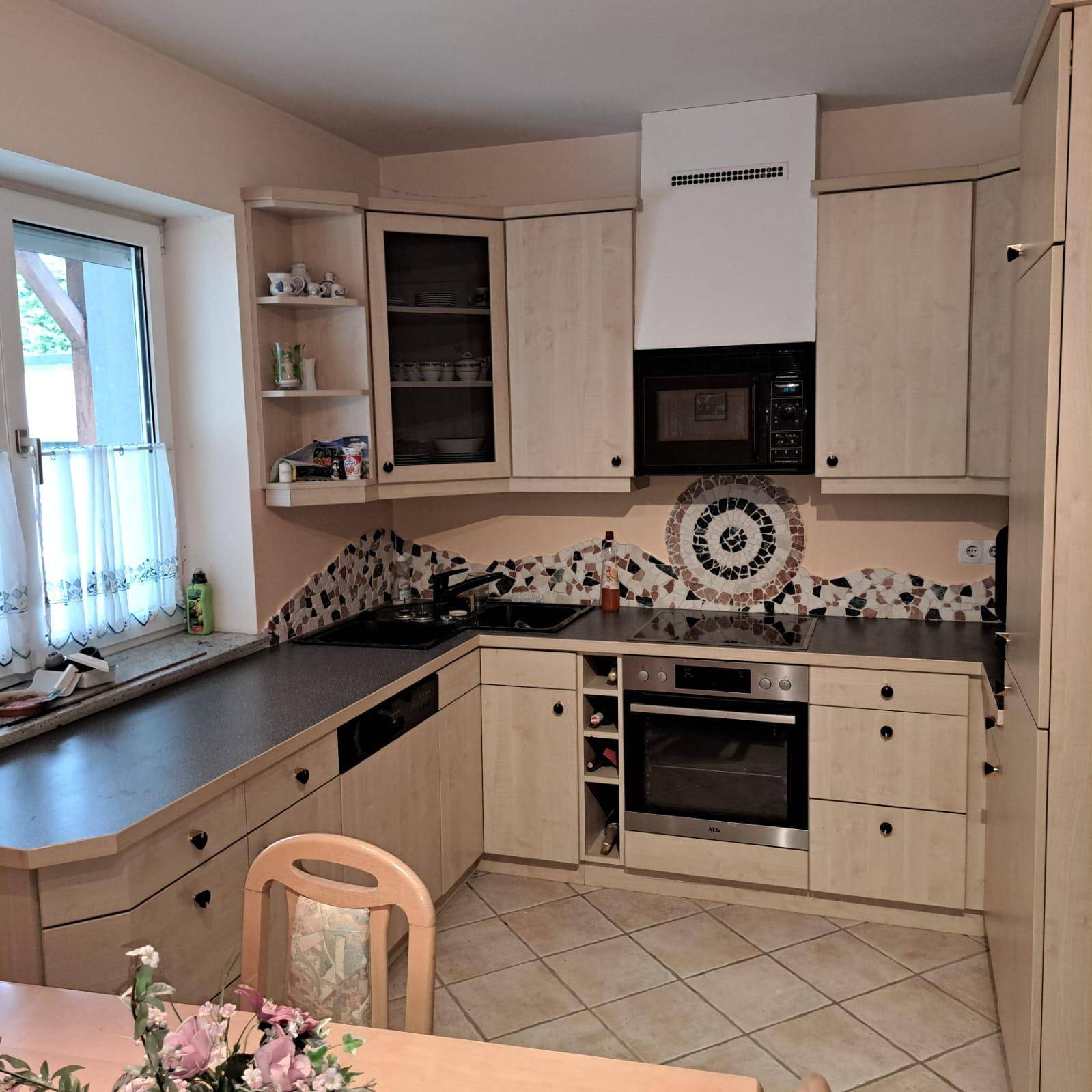 Helle Einbauküche mit Holzfronten, Fliesenboden und Fenster mit Blick nach draußen.