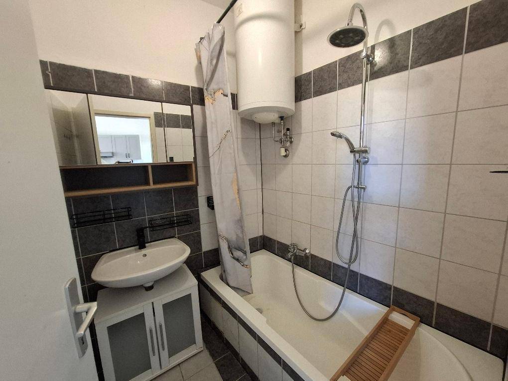Badezimmer mit Badewanne, Dusche, Waschbecken und Fliesen in Weiß und Dunkelgrau.