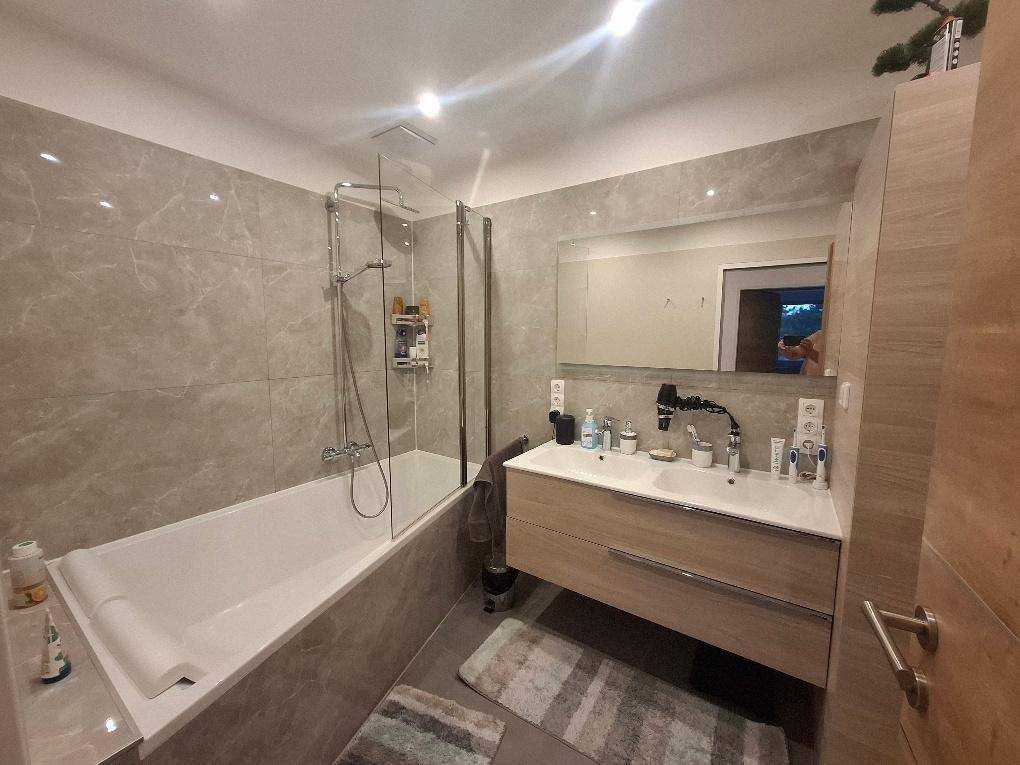 Modernes Badezimmer mit Badewanne, Duschabtrennung, Doppelwaschbecken und großen grauen Fliesen an den Wänden.
