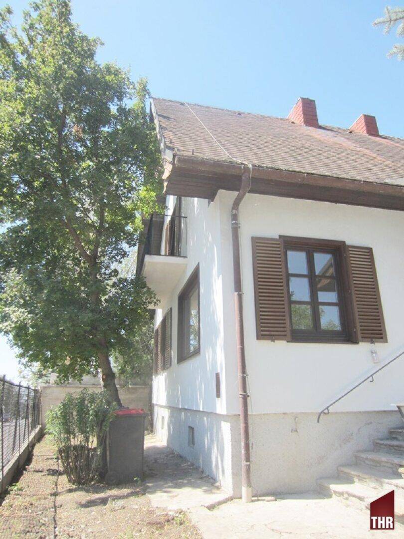 Seitenansicht des Hauses mit Fensterläden, Balkon und Zugang zum Gartenbereich.