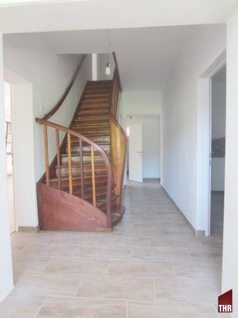 Geräumiger Flur mit Fliesenboden und einer geschwungenen Holztreppe ins Obergeschoss.