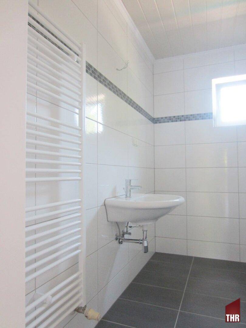Modern gefliestes Badezimmer mit Waschbecken, beheiztem Handtuchhalter und kleinem Fenster.