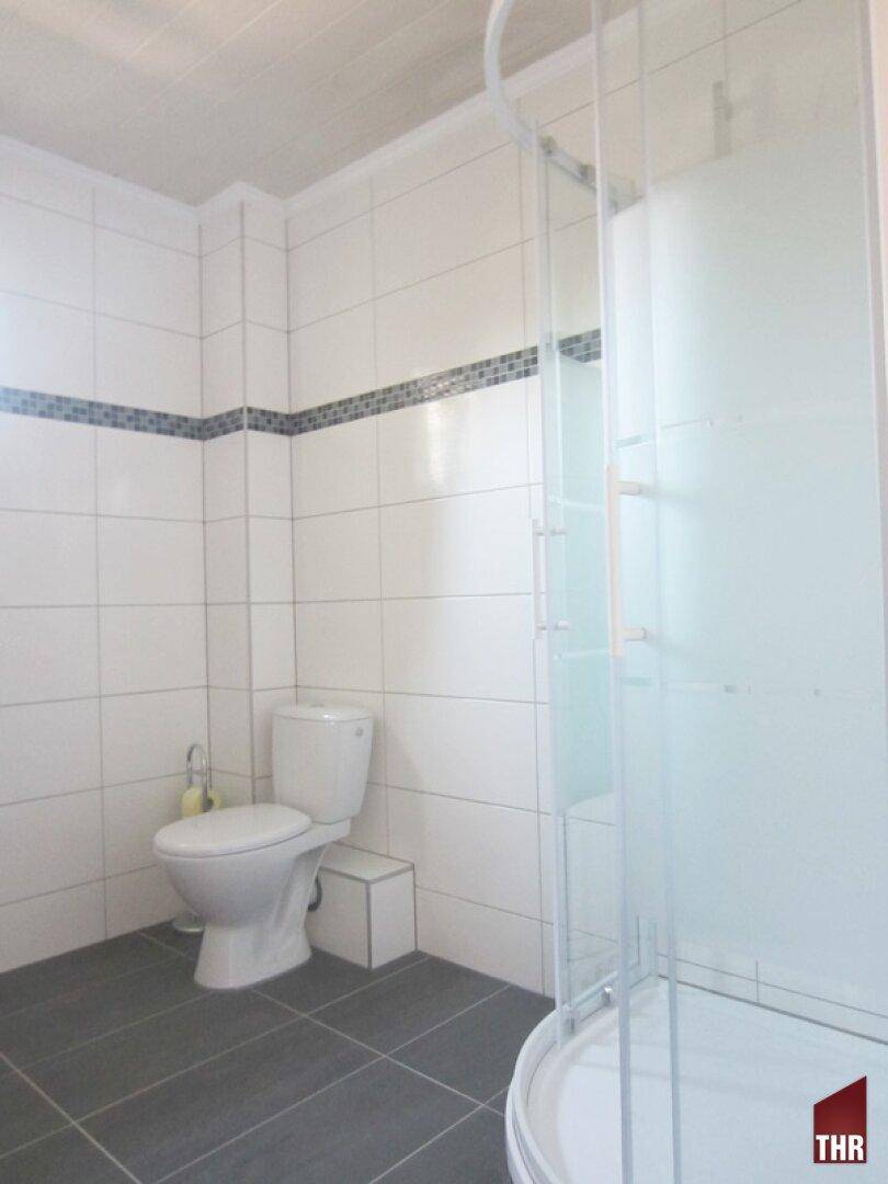 Gefliestes Badezimmer mit Toilette und Duschkabine, in hellen und dunklen Grautönen gehalten.