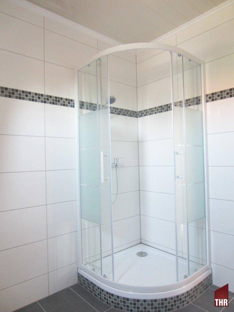 Badezimmer mit moderner Duschkabine und weißen Fliesen, akzentuiert durch eine Bordüre.