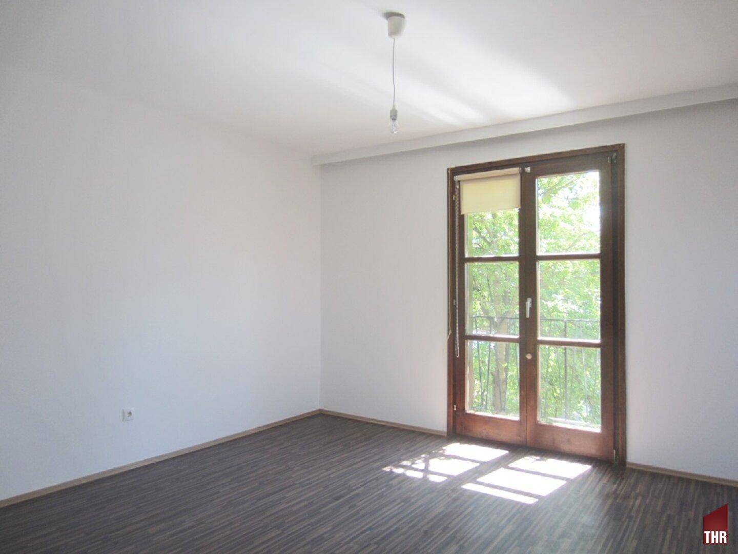 Helles Schlafzimmer mit Laminatboden und direktem Zugang zu einem kleinen Balkon.