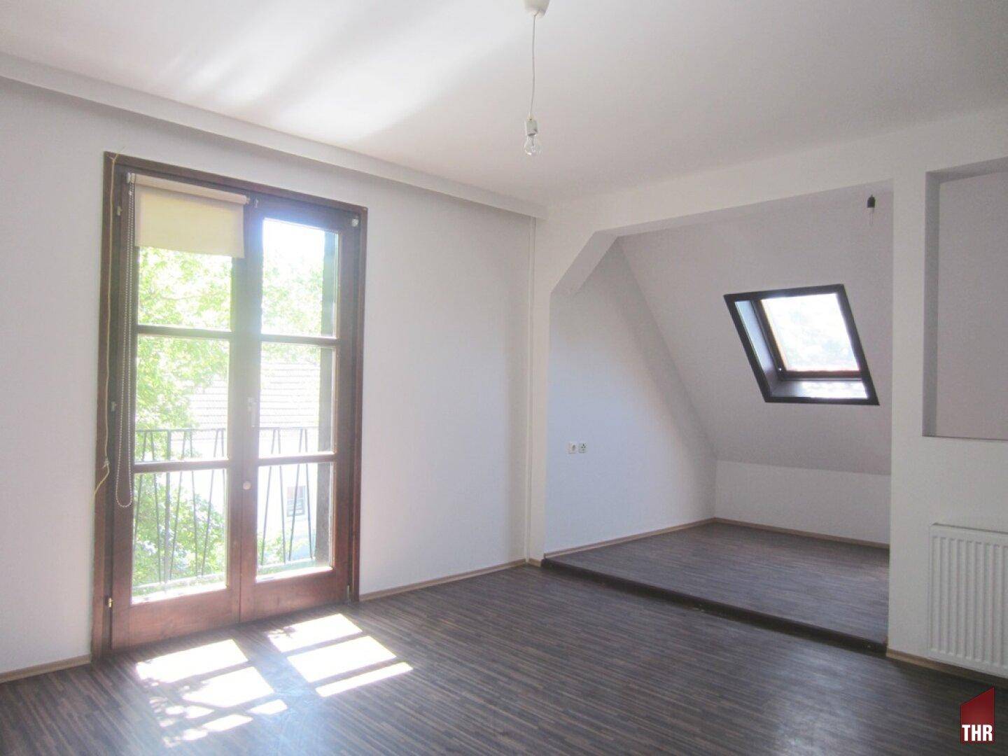 Helles Schlafzimmer im Dachgeschoss mit Holzboden, Balkonzugang und Dachfenster.