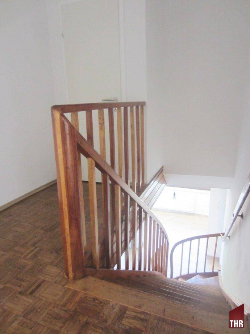 Blick von oben auf die geschwungene Holztreppe mit Holzgeländer, die nach unten führt.