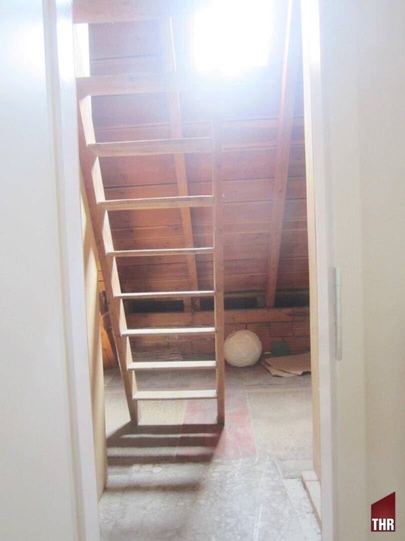 Zugang zum Dachboden über eine Holzleiter, mit sichtbarer Holzkonstruktion und Tageslicht.