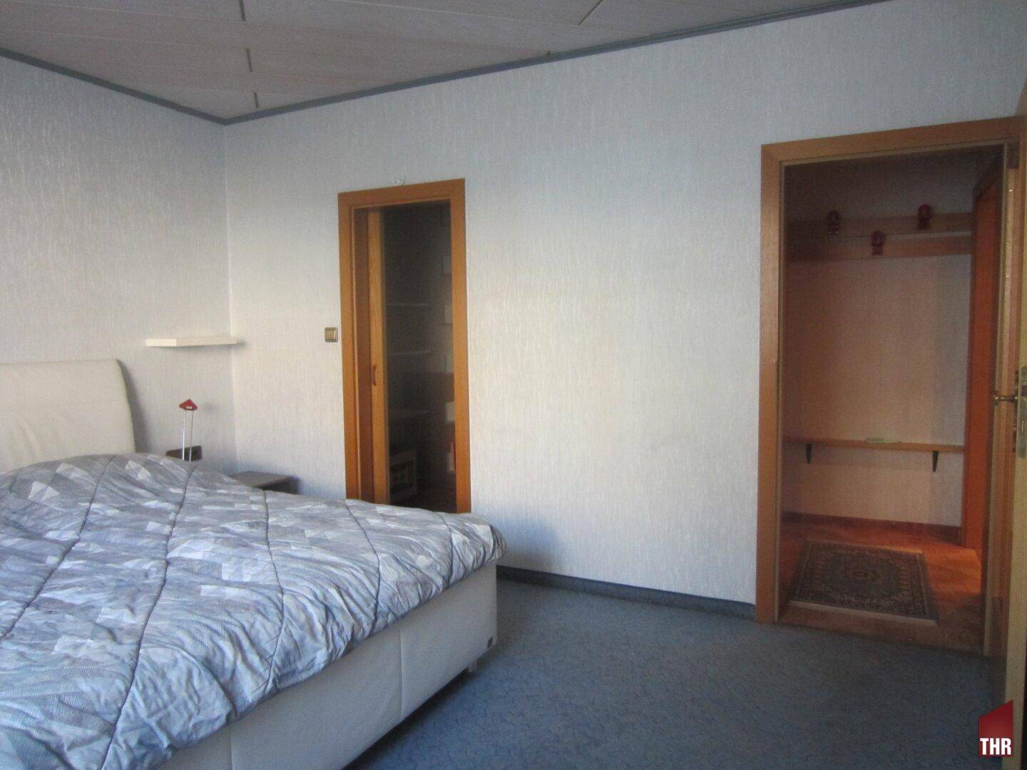 Schlafzimmer mit Teppichboden, hellem Bett und Zugang zu einem praktischen Schrankraum für Kleidung.