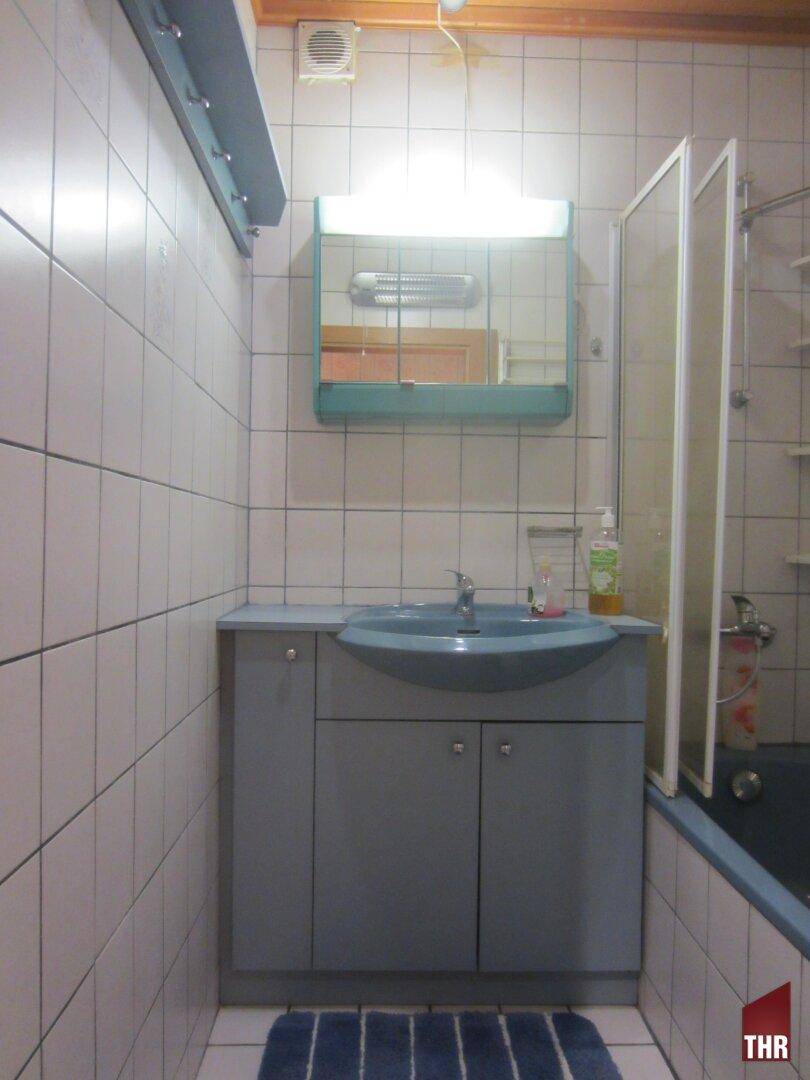 Badezimmer mit blauen Akzenten, weißen Fliesen und Badewanne mit Duschabtrennung, im Stil der 80er Jahre.