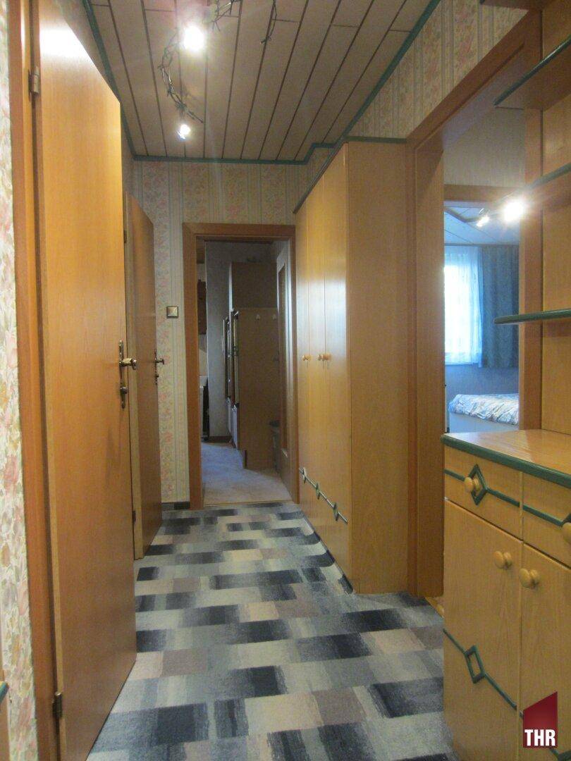 Langer Flur mit gemustertem Boden, Holzvertäfelung an der Decke und funktionalen Einbauschränken, die viel Stauraum bieten.