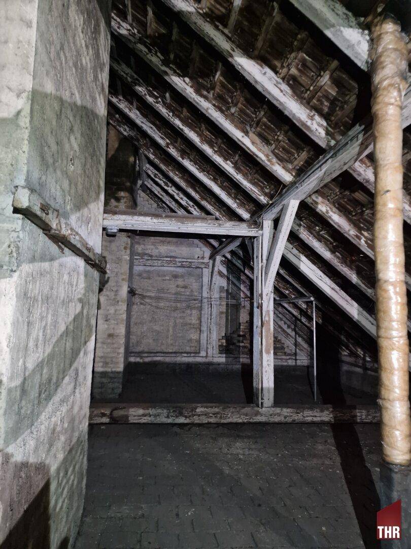 Geräumiger Dachboden mit freiliegenden Holzbalken und der ursprünglichen Dachkonstruktion, in dunkler Atmosphäre.