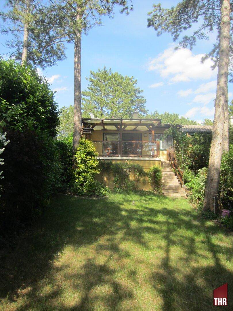 Ansicht des Hauses von der Gartenseite mit einer überdachten Terrasse und umgebenden Bäumen.