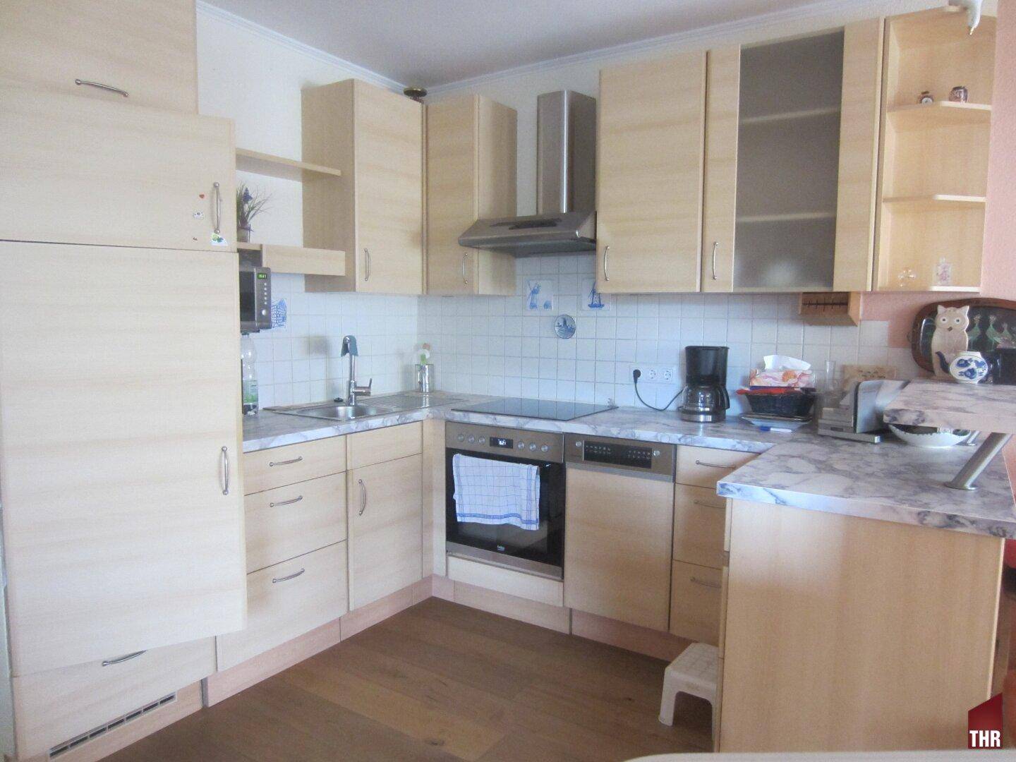 Helle Einbauküche mit hellen Holzfronten, modernen Geräten und Fliesenboden.