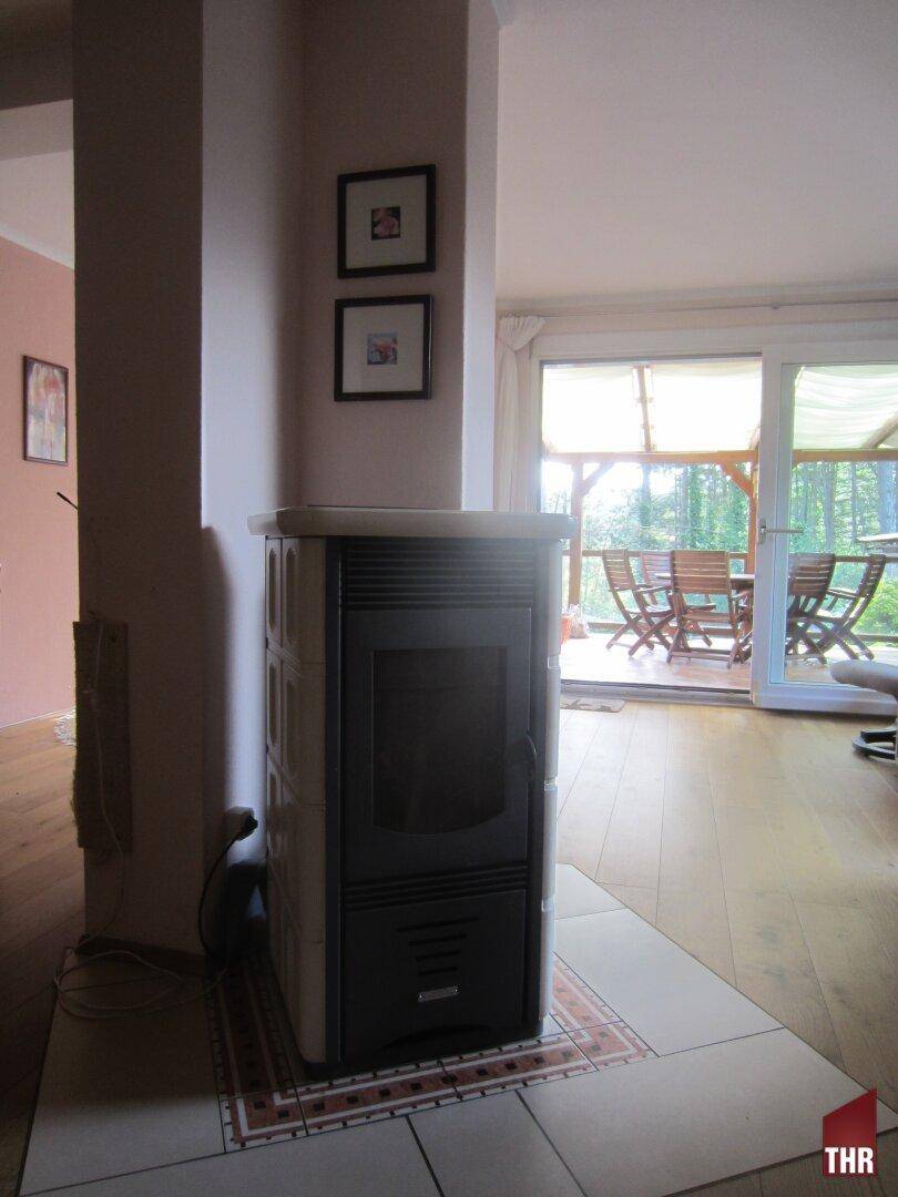 Gemütlicher Wohnbereich mit Kaminofen und Zugang zu einer überdachten Terrasse mit Waldblick.