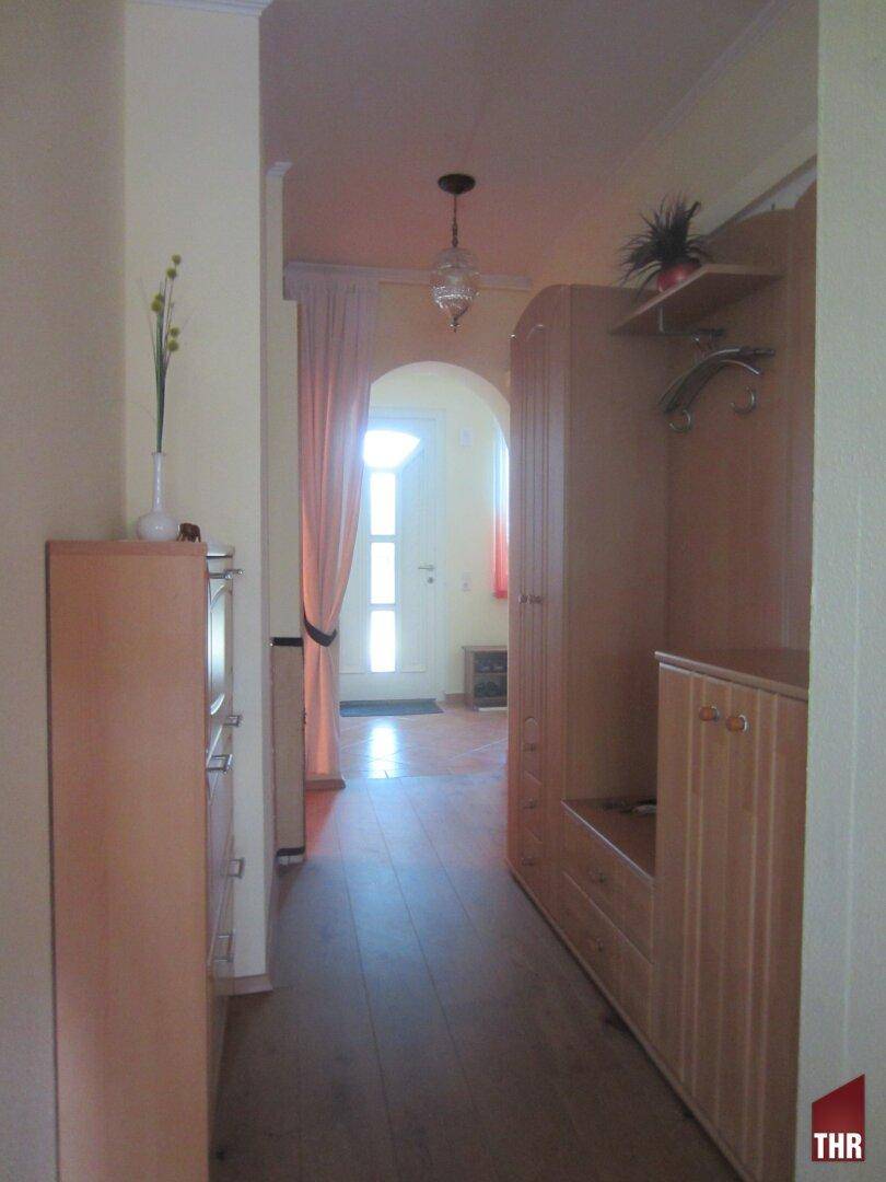 Heller Flur mit Holzmöbeln und Garderobe, der zum Eingangsbereich führt.