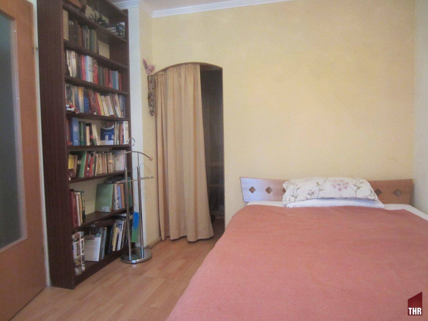 Schlafzimmer mit Holzboden, Bücherregal und einem Vorhang, der einen weiteren Bereich abtrennt.