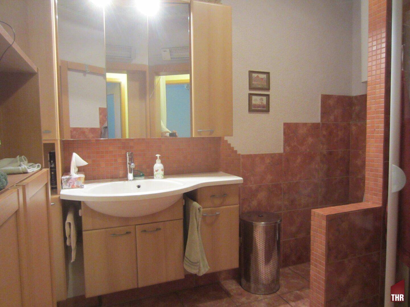 Badezimmer mit Waschtisch, Spiegelschrank und braunen Fliesen an Wänden und Boden.
