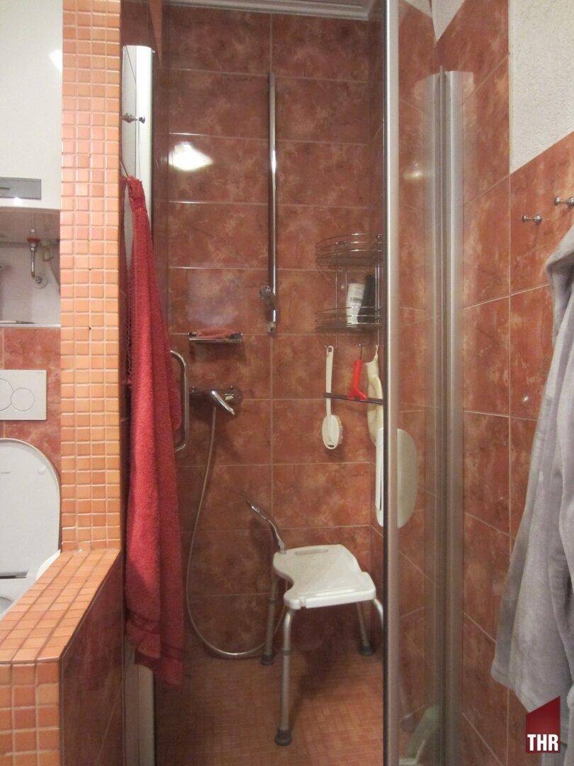 Duschbereich im Badezimmer mit braunen Fliesen und einer Duschkabine mit Sitzgelegenheit.