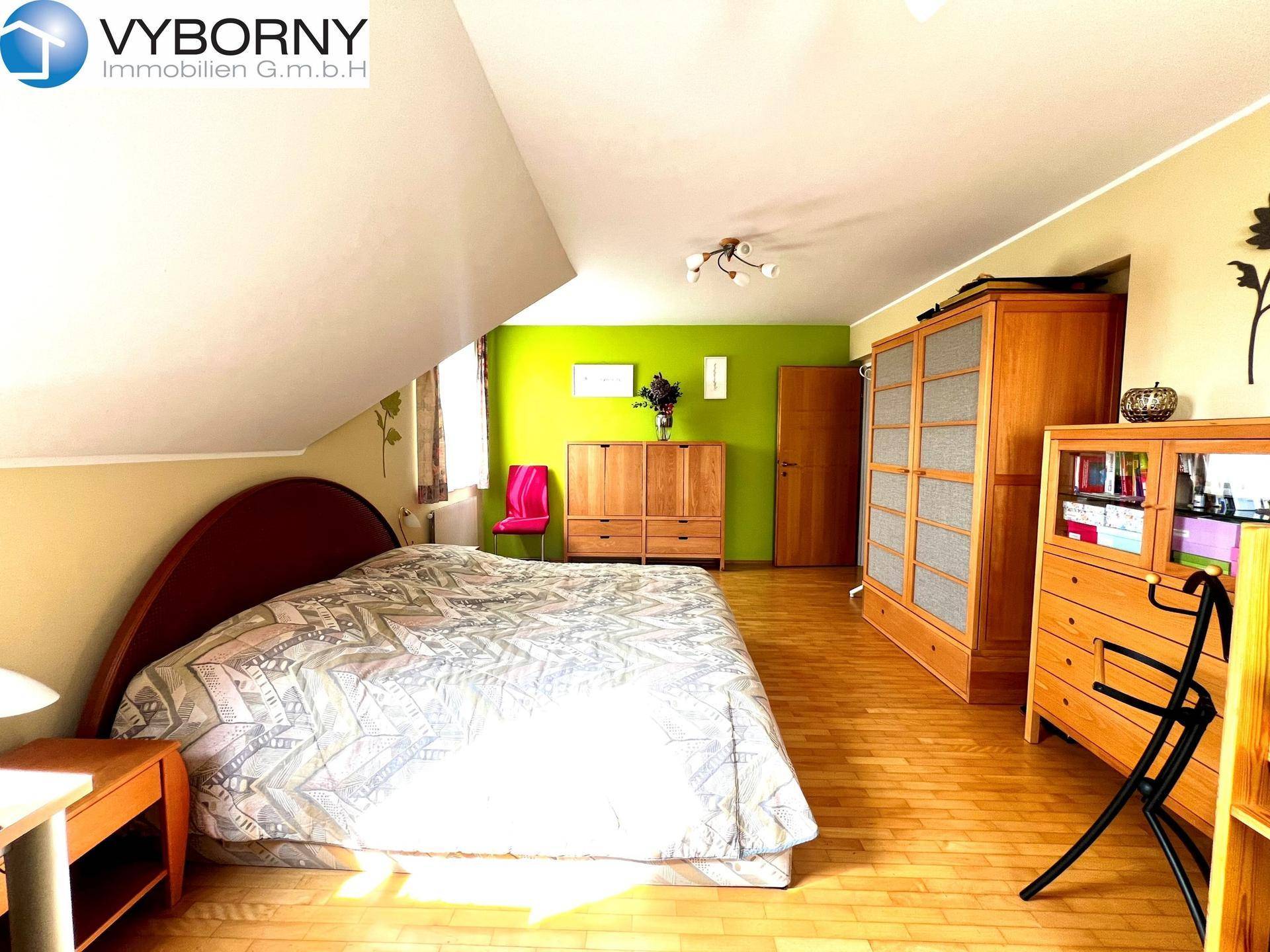 Geräumiges Schlafzimmer mit Holzboden, Dachschrägen und einer grünen Akzentwand.