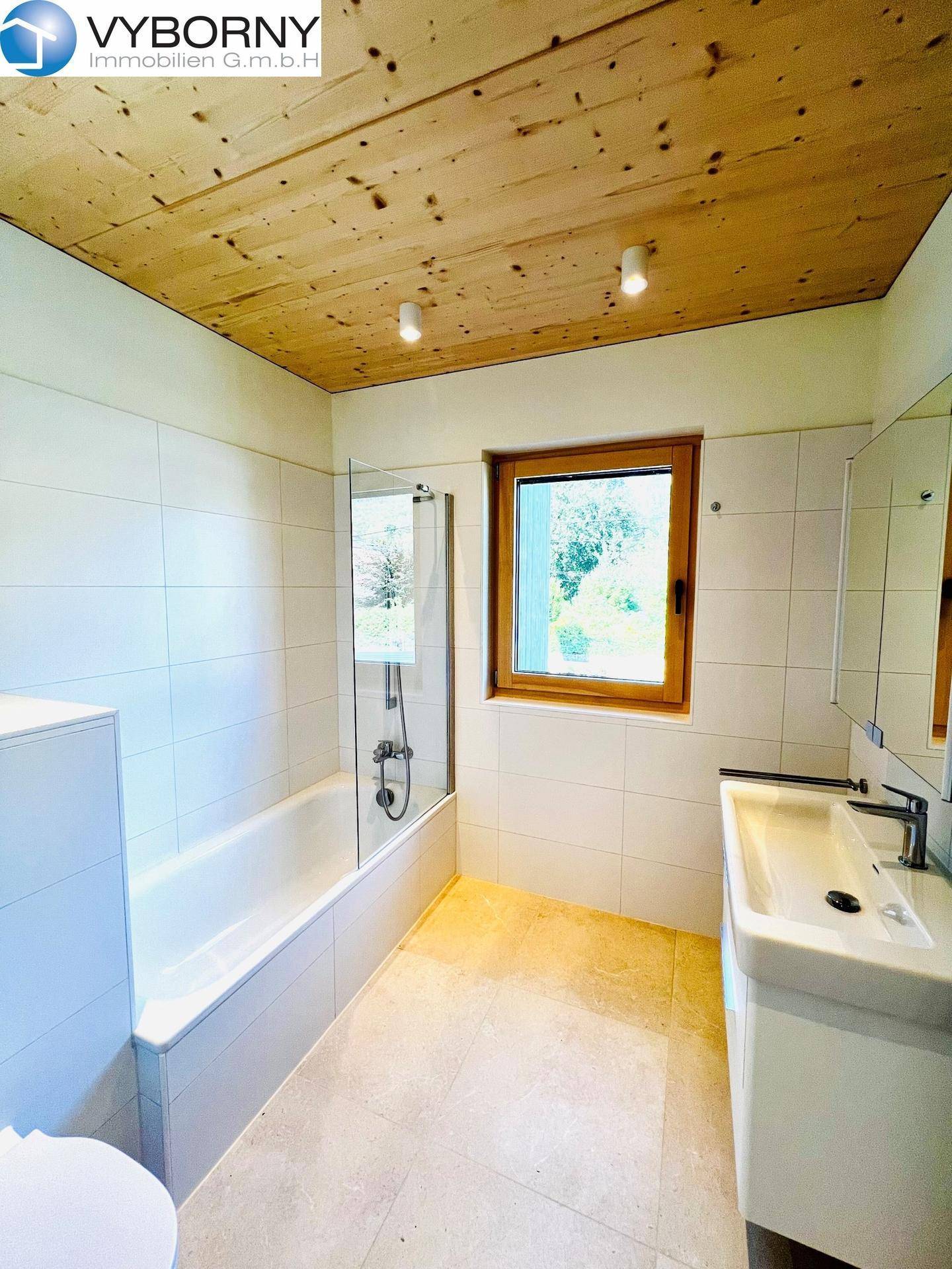 Modernes Badezimmer mit Badewanne, Duschabtrennung, Fenster und Holzdecke.