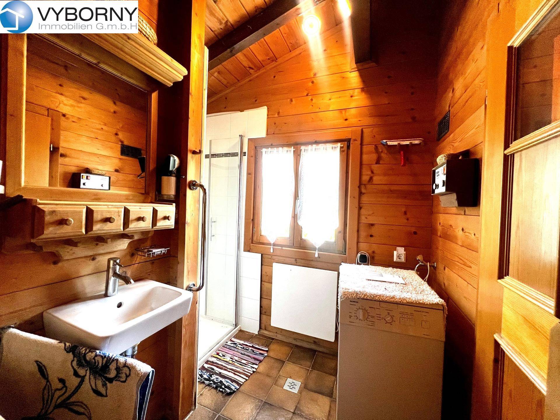 Kleines Badezimmer mit Dusche, Waschbecken und Waschmaschine in Holzvertäfelung.