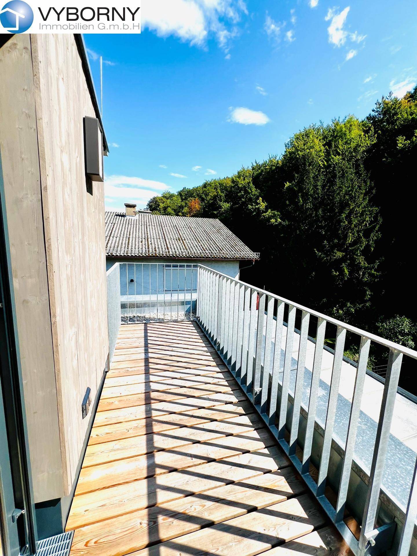 Schmaler Holzbalkon mit Metallgeländer und sonnigem Ausblick auf die Umgebung.