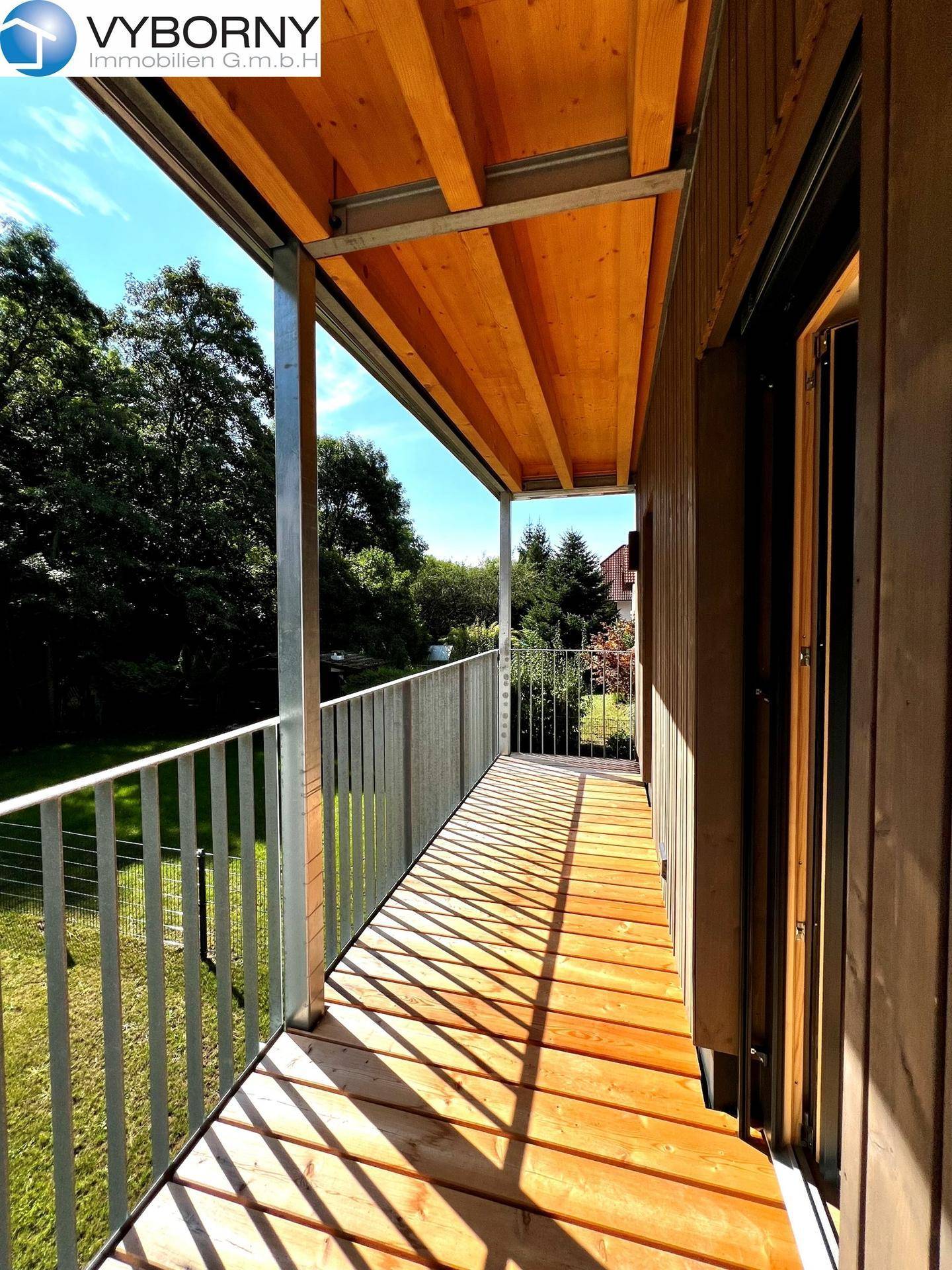 Langer Holzbalkon mit Metallgeländer und Blick auf die umliegende grüne Landschaft.