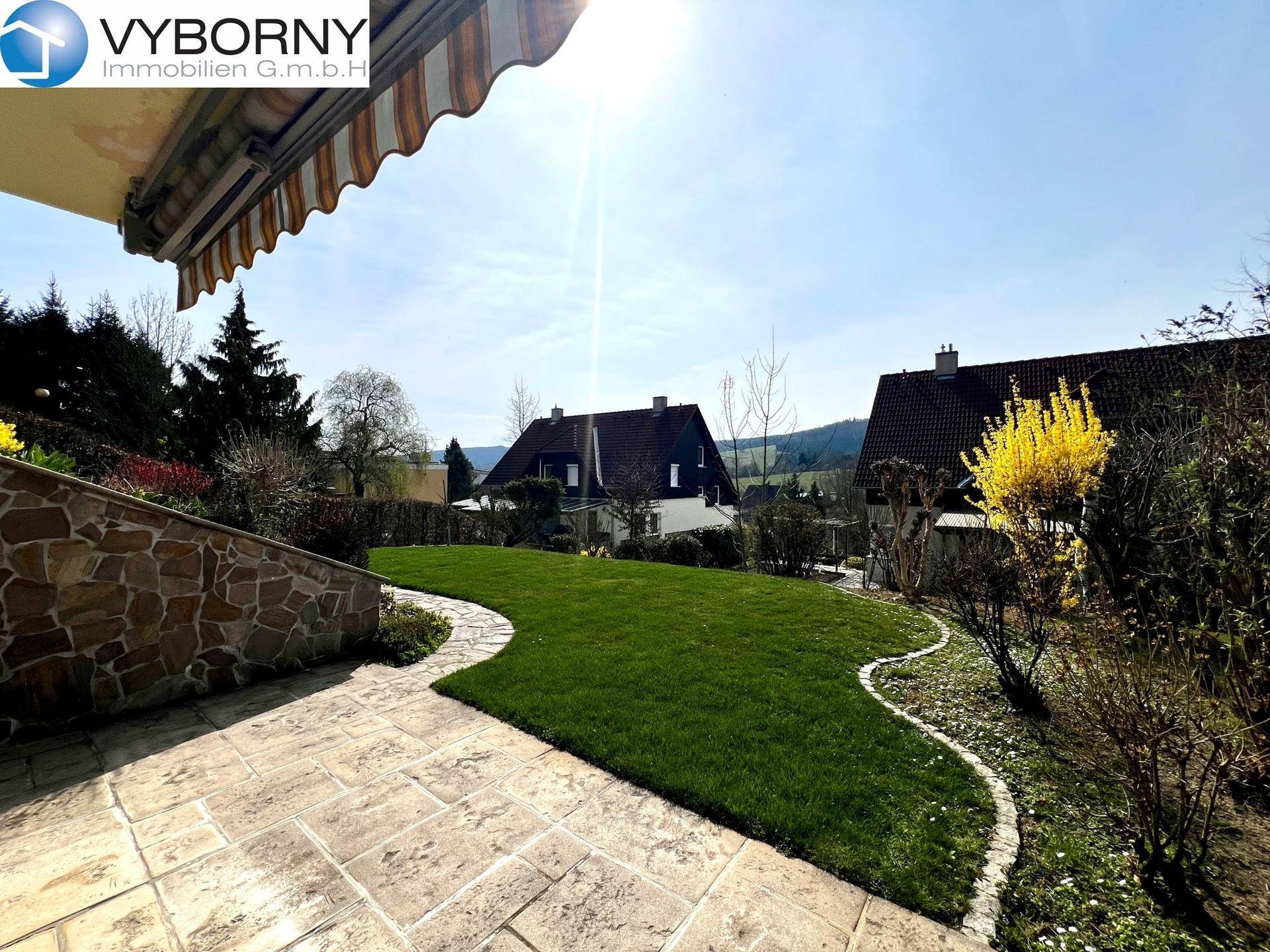 Gepflasterte Terrasse mit Markise und Blick auf den Garten und die umliegende Landschaft.