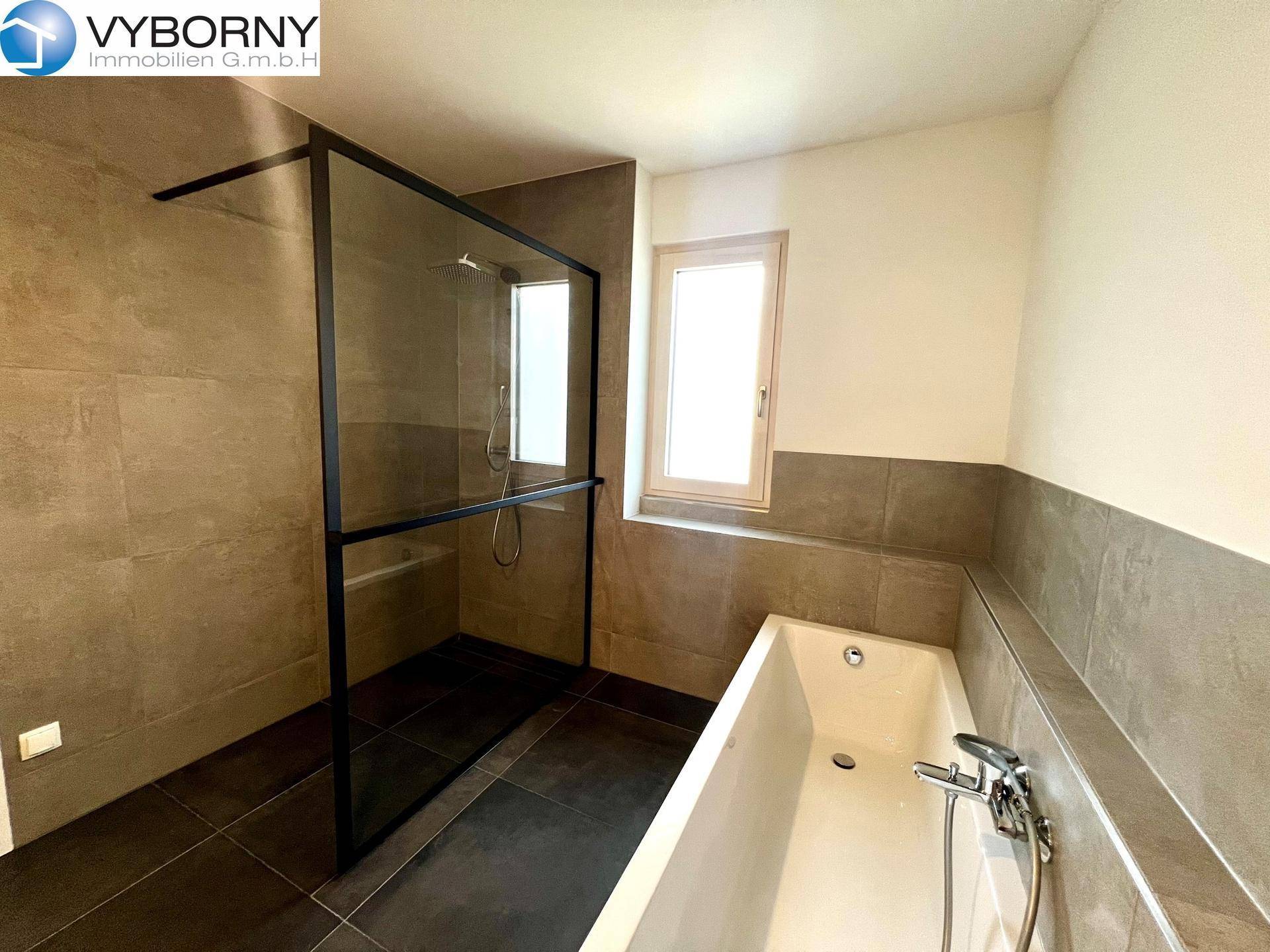 Elegantes Badezimmer mit begehbarer Dusche, Badewanne und modernen grauen Fliesen.