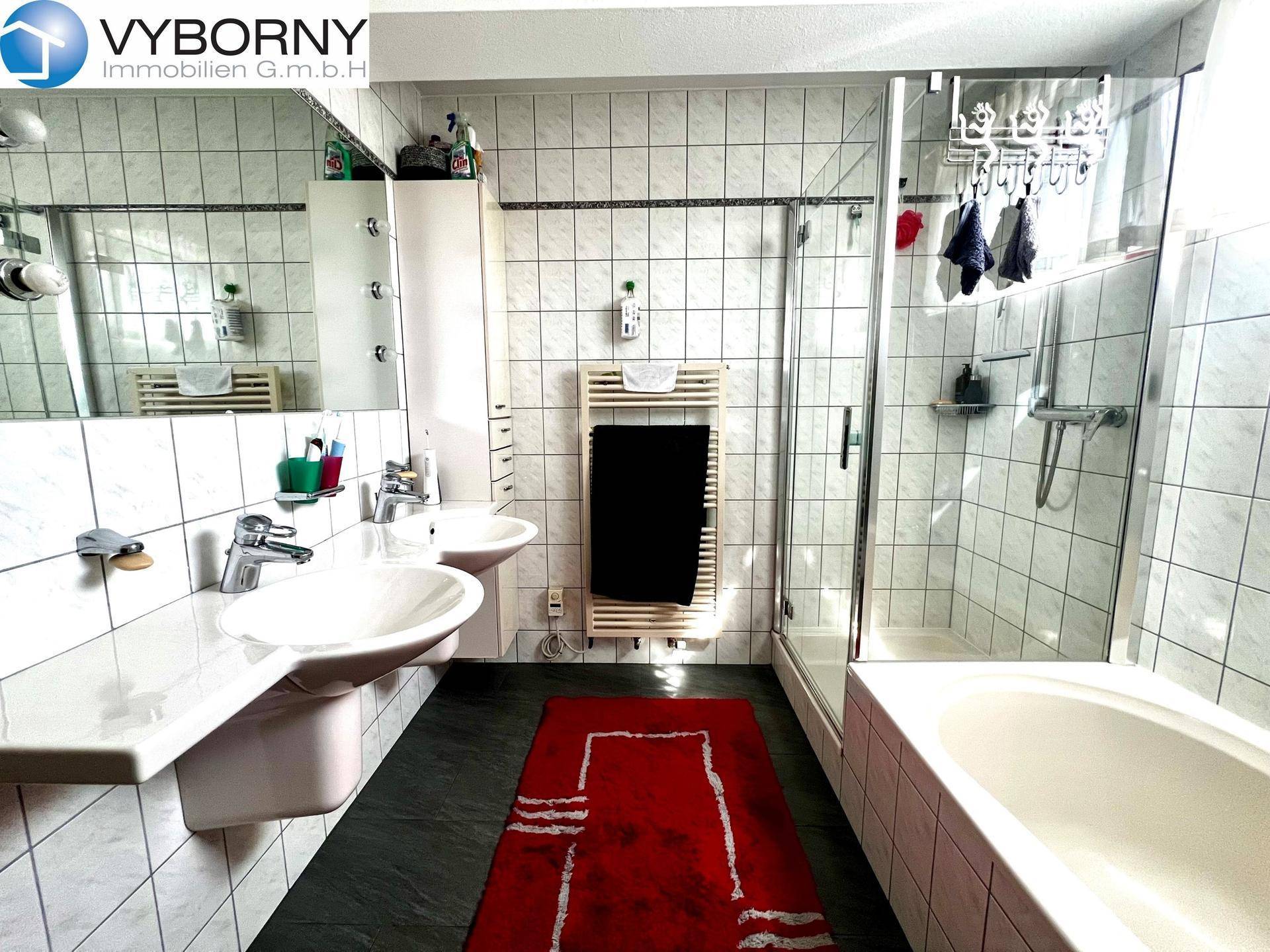 Badezimmer mit Doppelwaschbecken, Badewanne, Duschkabine und Fliesen an Wänden und Boden.