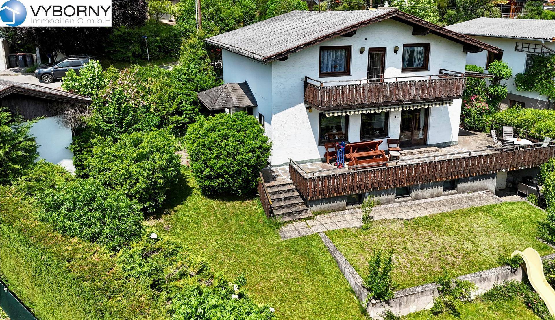 Hausansicht von oben mit Balkon, großer Terrasse und weitläufigem Gartenbereich mit Rasenfläche.