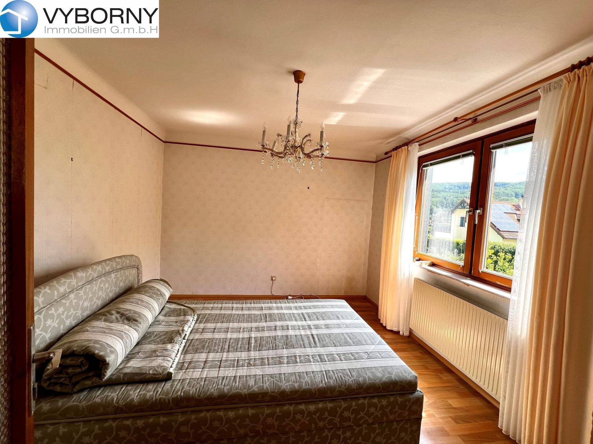 Schlafzimmer mit Doppelbett, Kronleuchter und großem Fenster mit Ausblick ins Grüne.