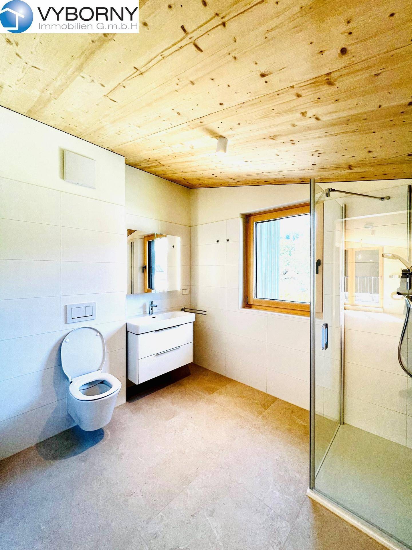 Helles Badezimmer mit begehbarer Dusche, WC, Waschbecken und Fenster.