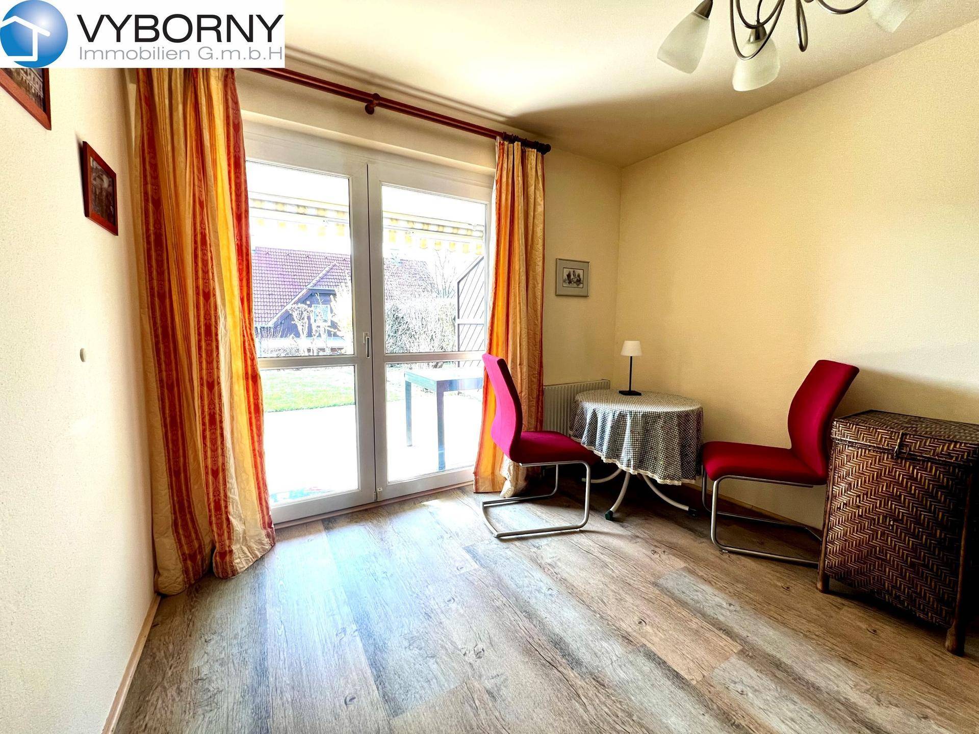 Helles Zimmer mit Laminatboden und direktem Zugang zum Garten durch eine Glastür.