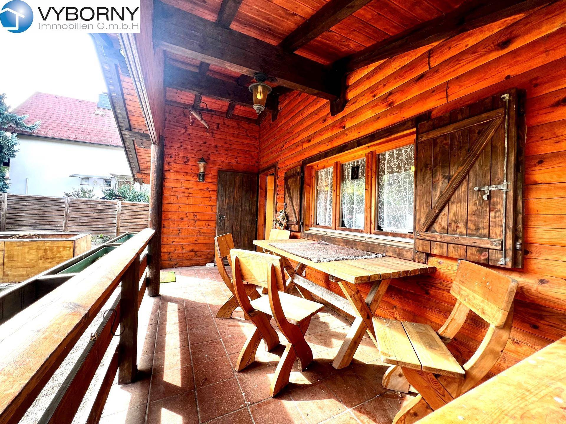 Überdachte Terrasse mit Holztisch und Stühlen, ideal für Mahlzeiten im Freien.