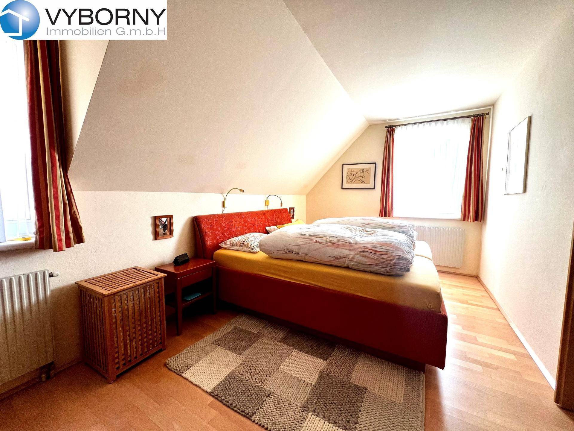 Schlafzimmer im Dachgeschoss mit Holzboden, rotem Bett und schrägen Wänden.