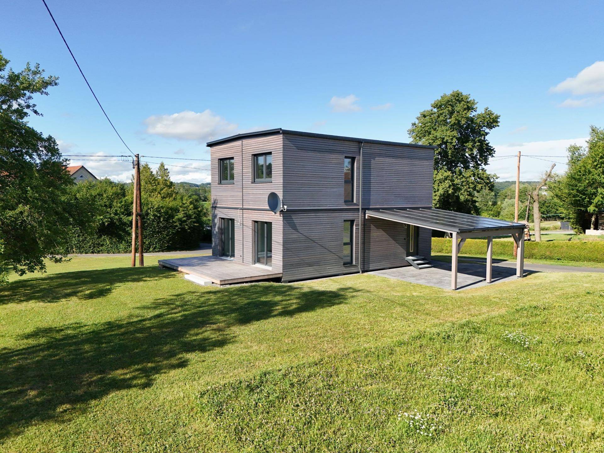 Modernes Wohnhaus mit Holzfassade, Carport mit Solaranlage und weitläufigem grünen Grundstück.