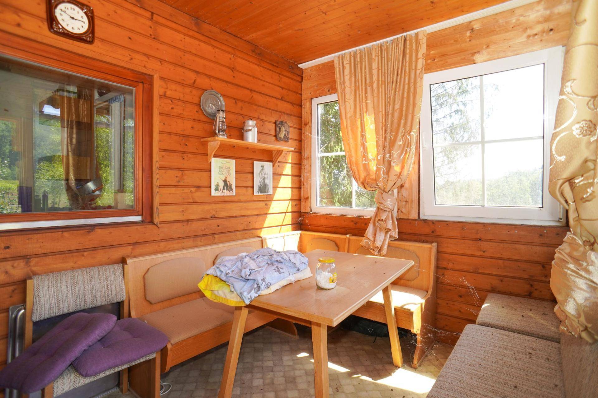 Gemütlicher, holzvertäfelter Raum mit Sitzbänken, Tisch und Fenstern mit Blick ins Grüne.