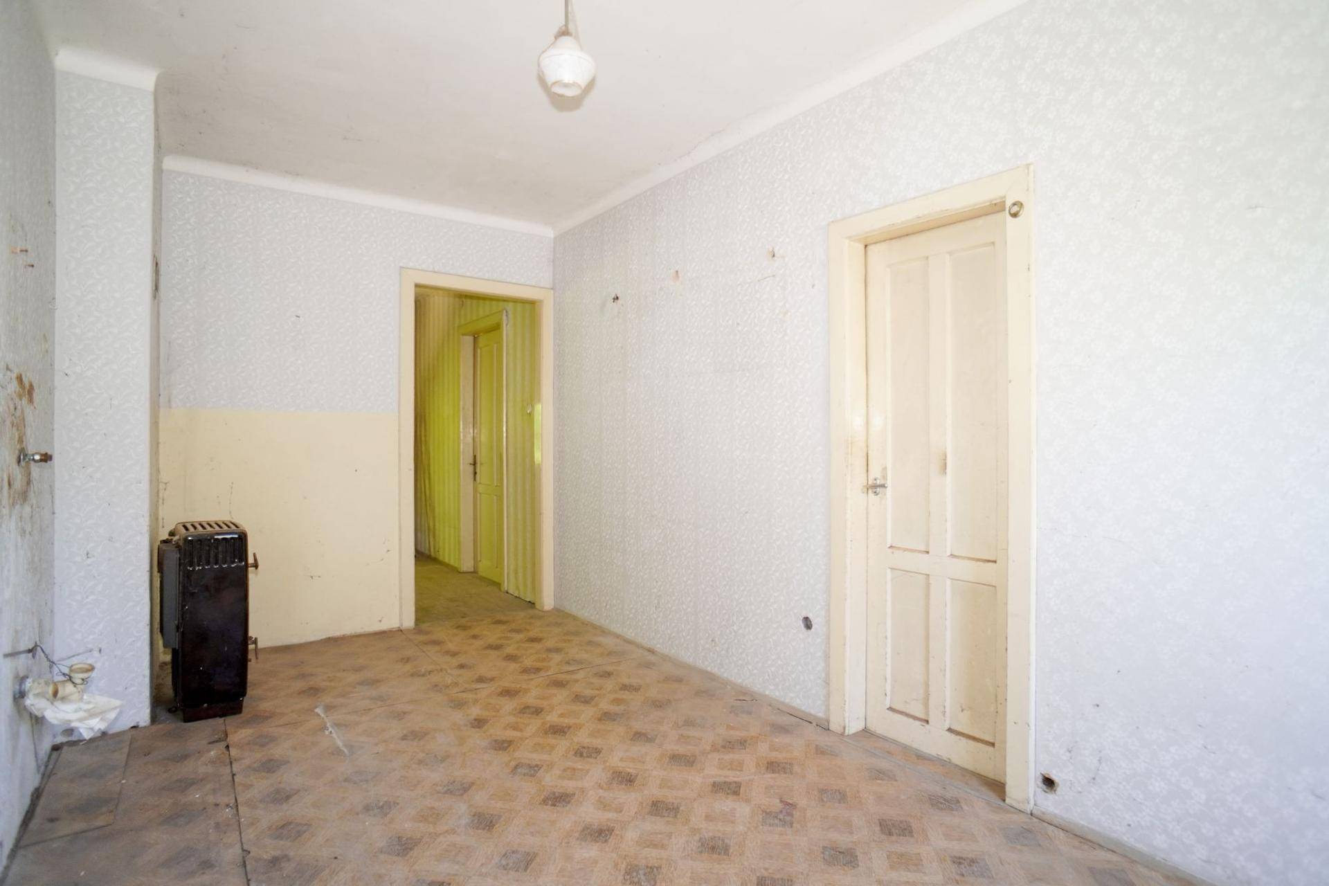 Raum mit altem Linoleumboden, Heizkörper und Zugang zu weiteren Zimmern.