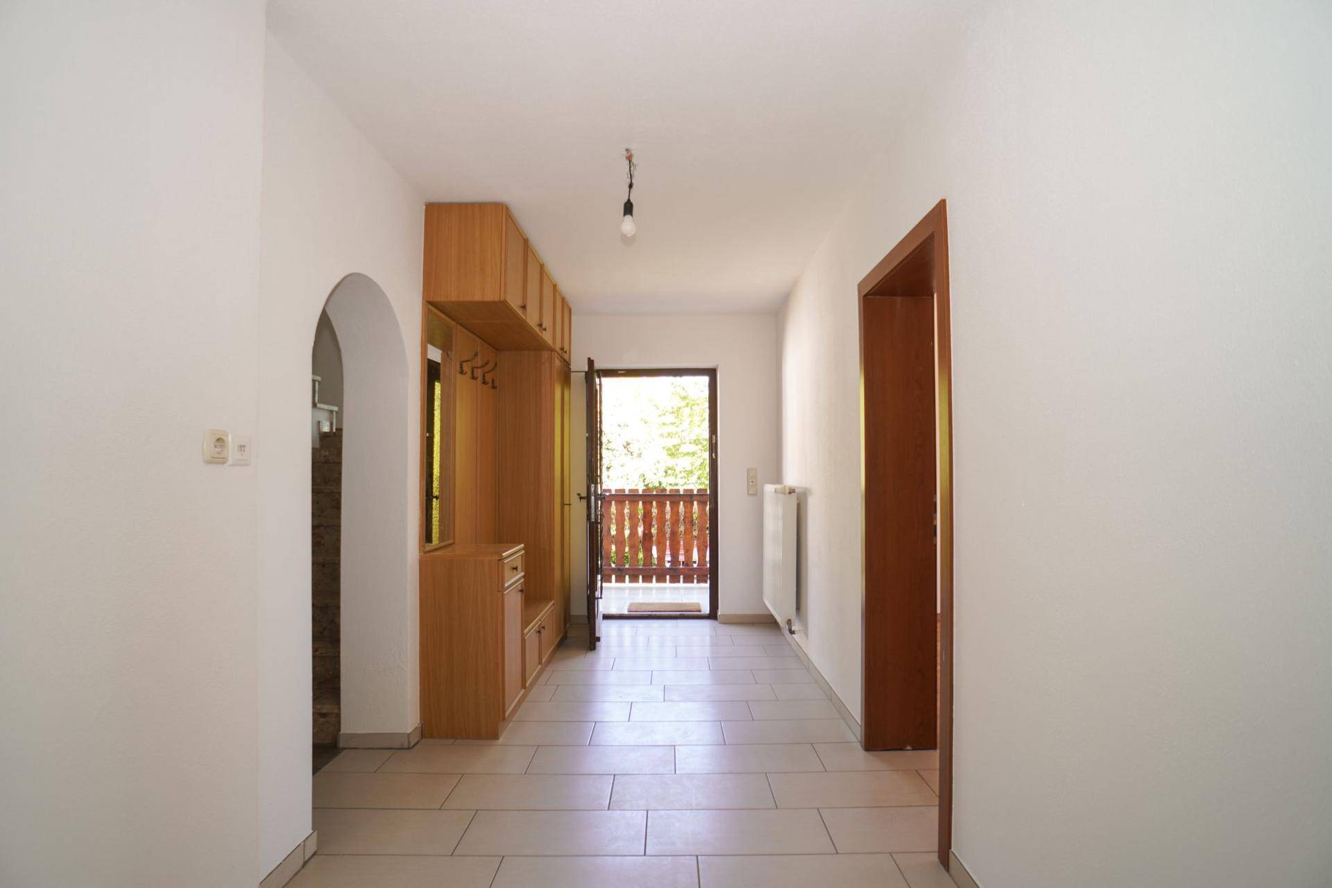 Heller Eingangsbereich mit Fliesenboden, Holzmöbeln und Zugang zum Balkon.