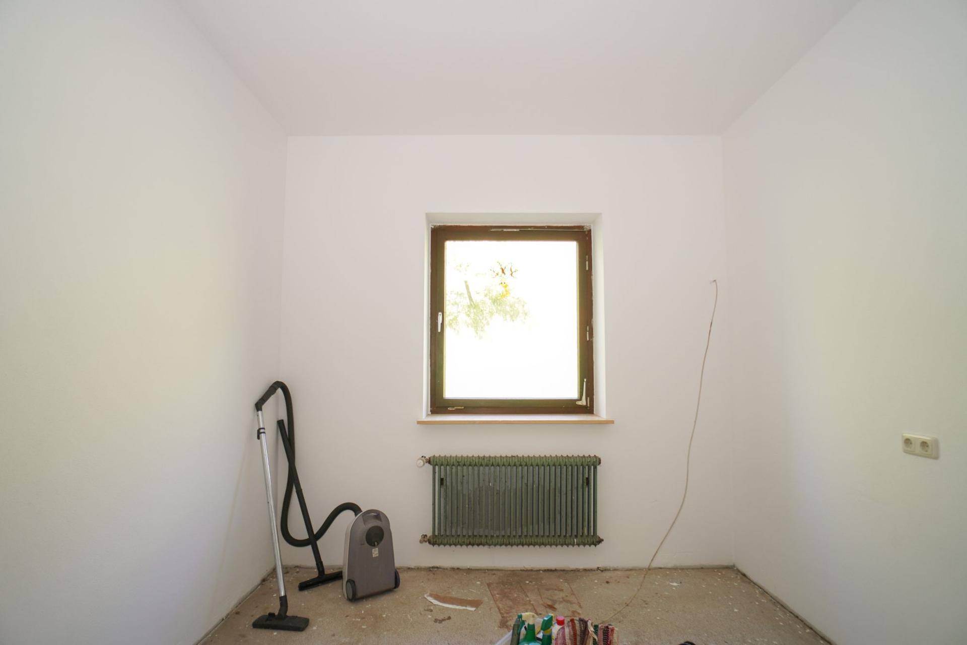 Leerer Raum mit einem Fenster und Heizkörper, bereit für Renovierung oder Einrichtung.
