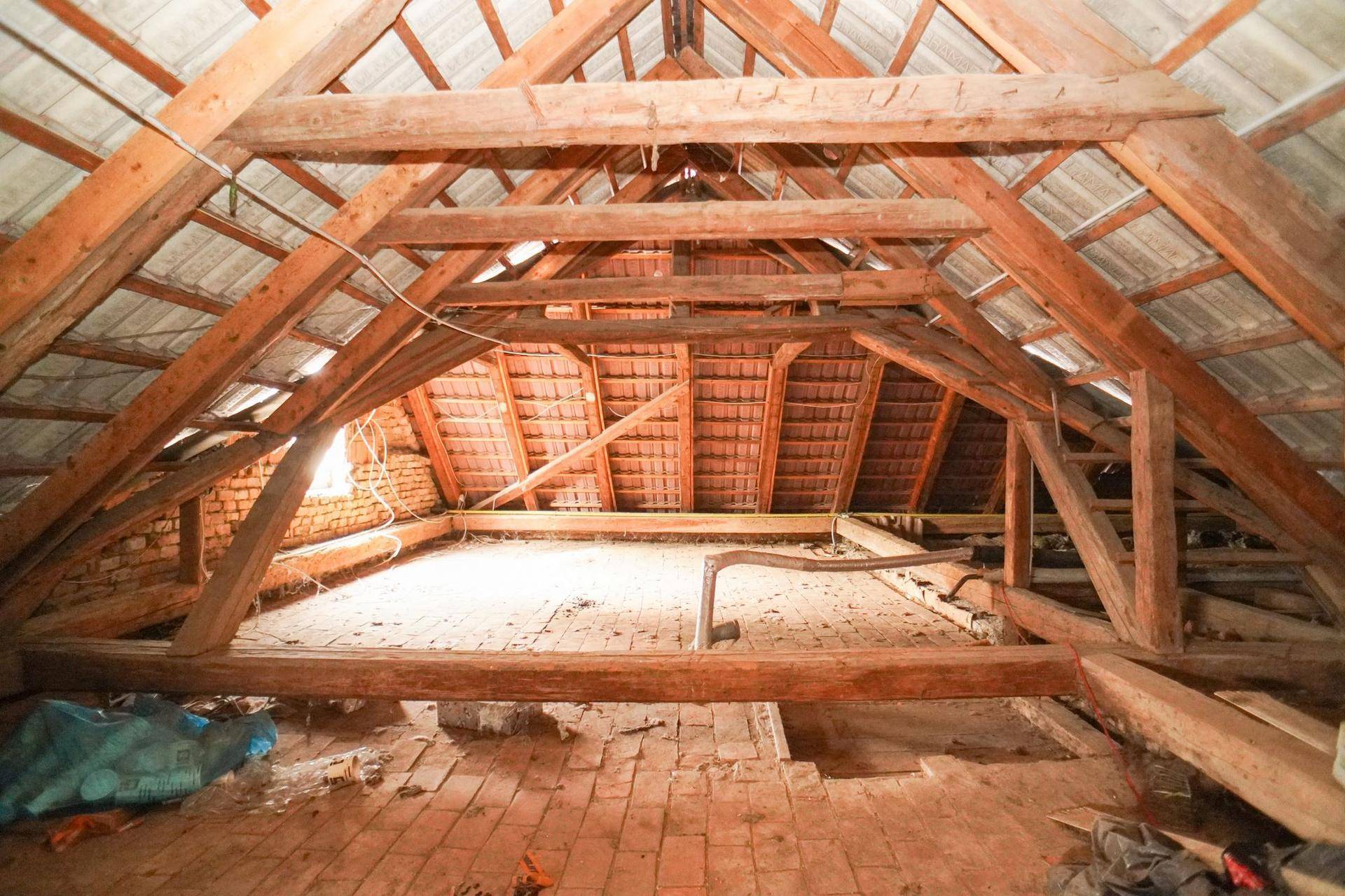 Dachboden mit sichtbarer Holzkonstruktion, Ziegelboden und natürlichem Lichteinfall.