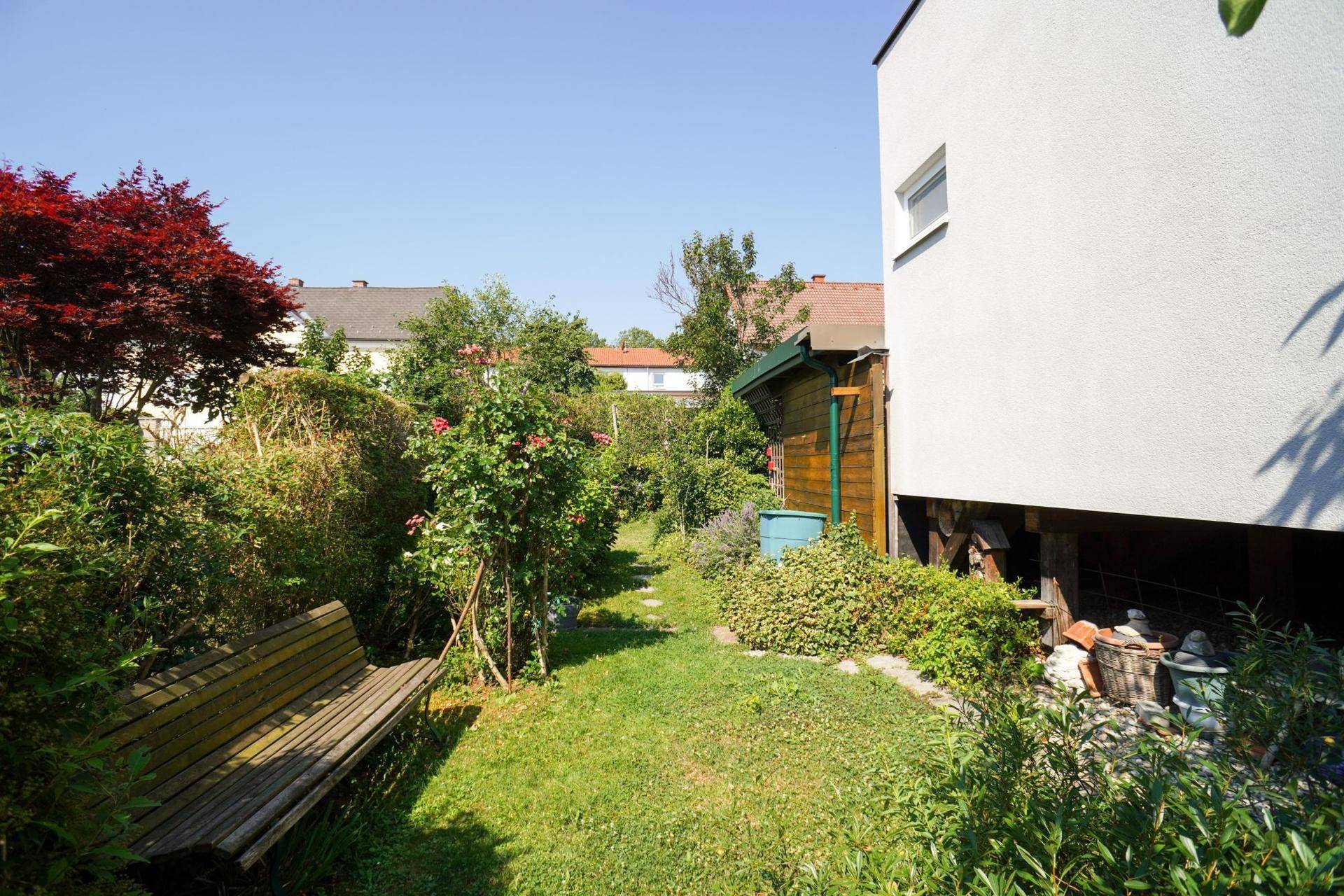 Idyllischer Gartenweg mit üppiger Bepflanzung und einer Holzbank zum Entspannen im Grünen.