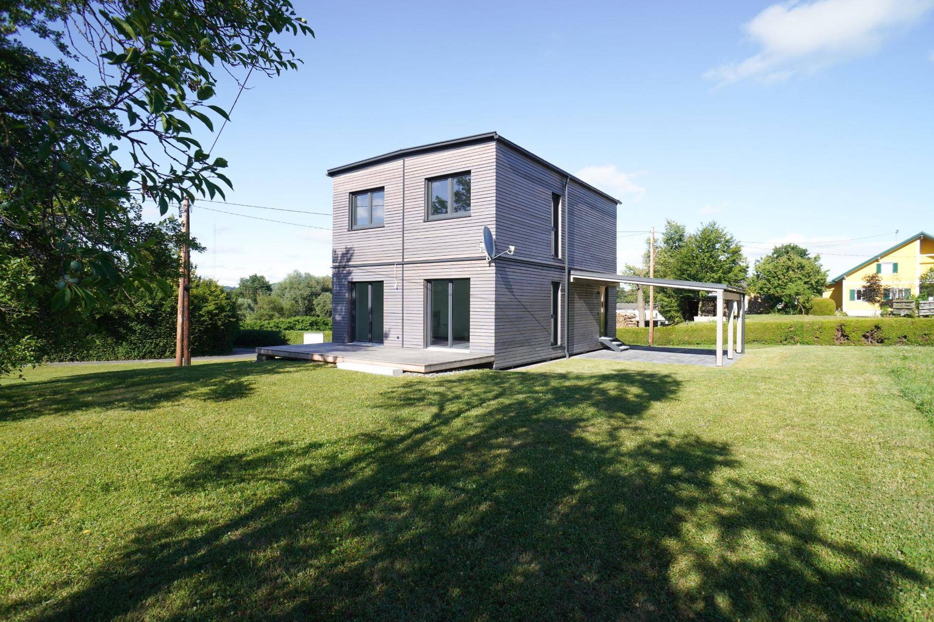 Freistehendes modernes Haus mit Holzverkleidung, Carport und weitläufigem Grundstück.