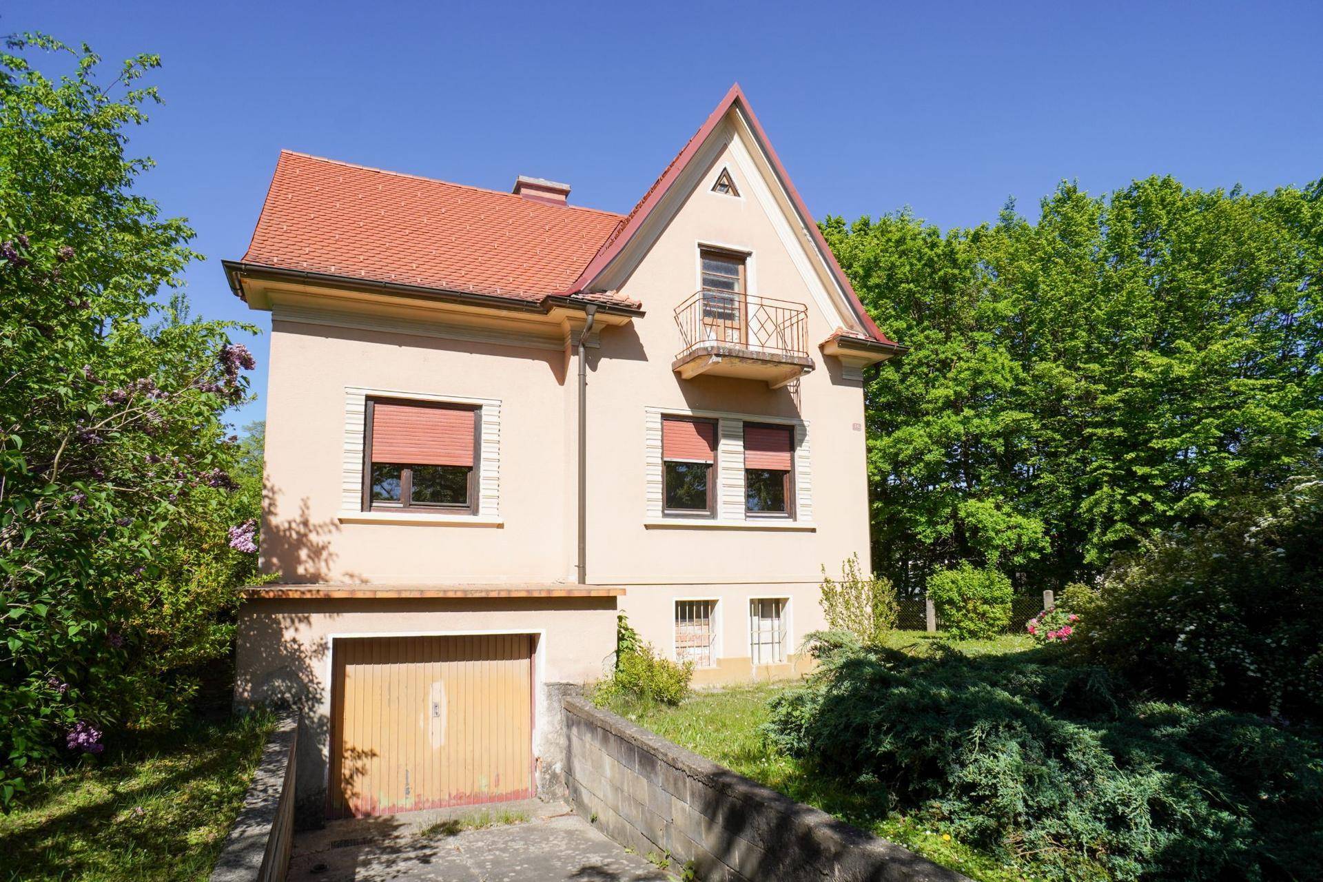 Ansicht des Hauses mit Garage, rotem Dach und üppigem Grün im Gartenbereich.