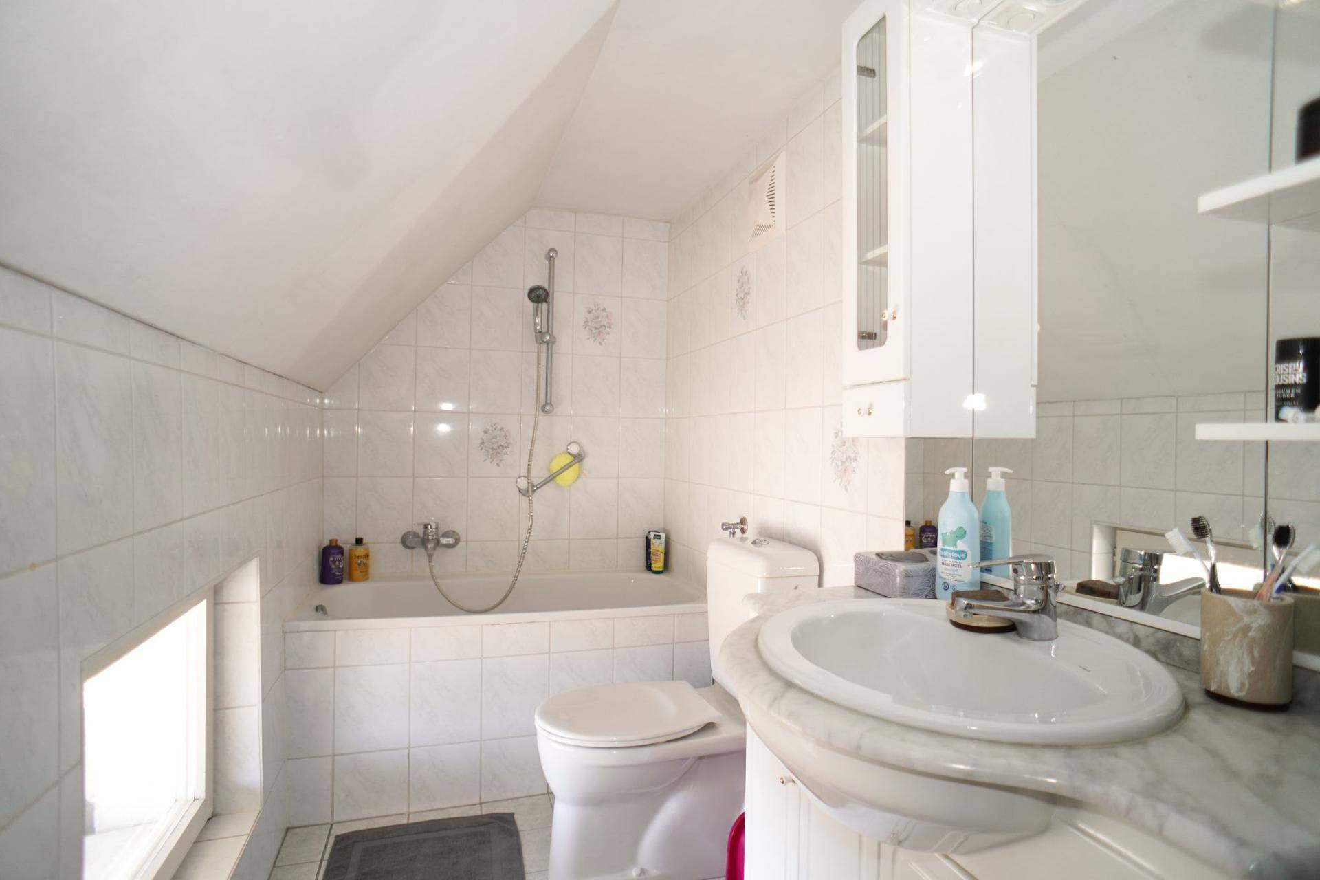Dachgeschoss-Badezimmer mit Badewanne, WC und Waschbecken unter einer Dachschräge.