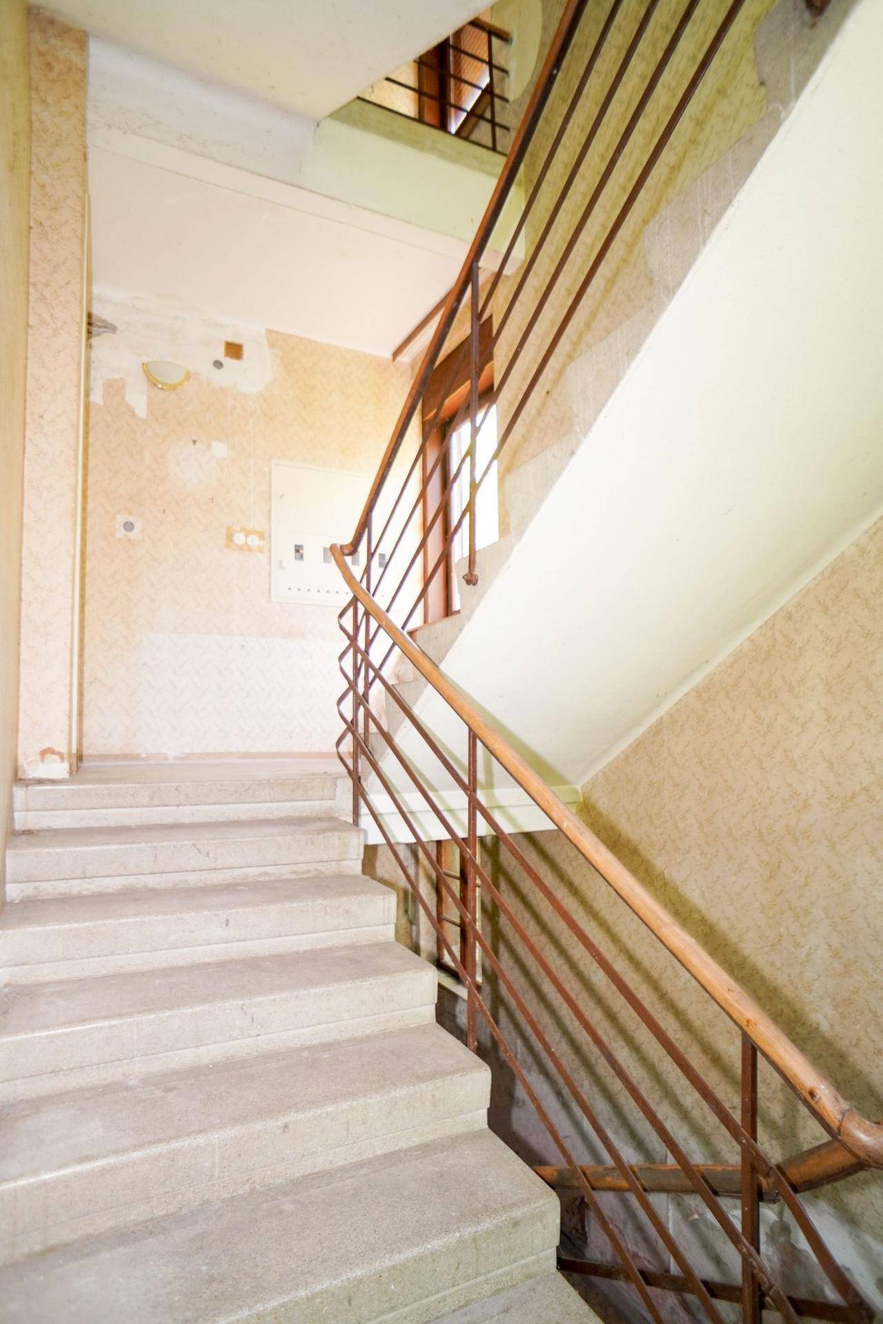 Treppenhaus mit Steinstufen und Metallgeländer, das Renovierungsbedarf aufweist.