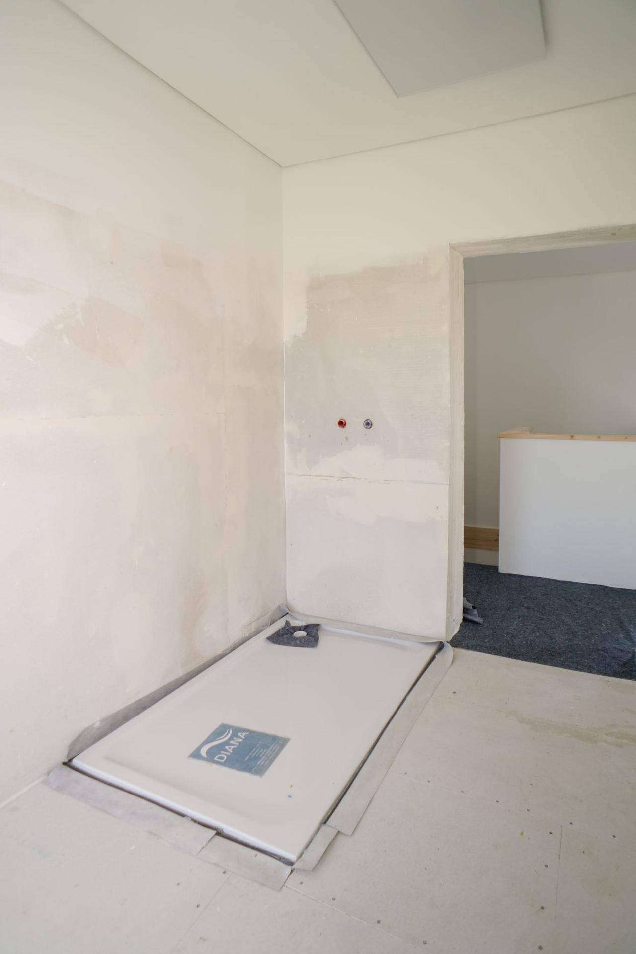 Unfertiges Badezimmer mit installierter Duschwanne und vorbereiteten Anschlüssen.