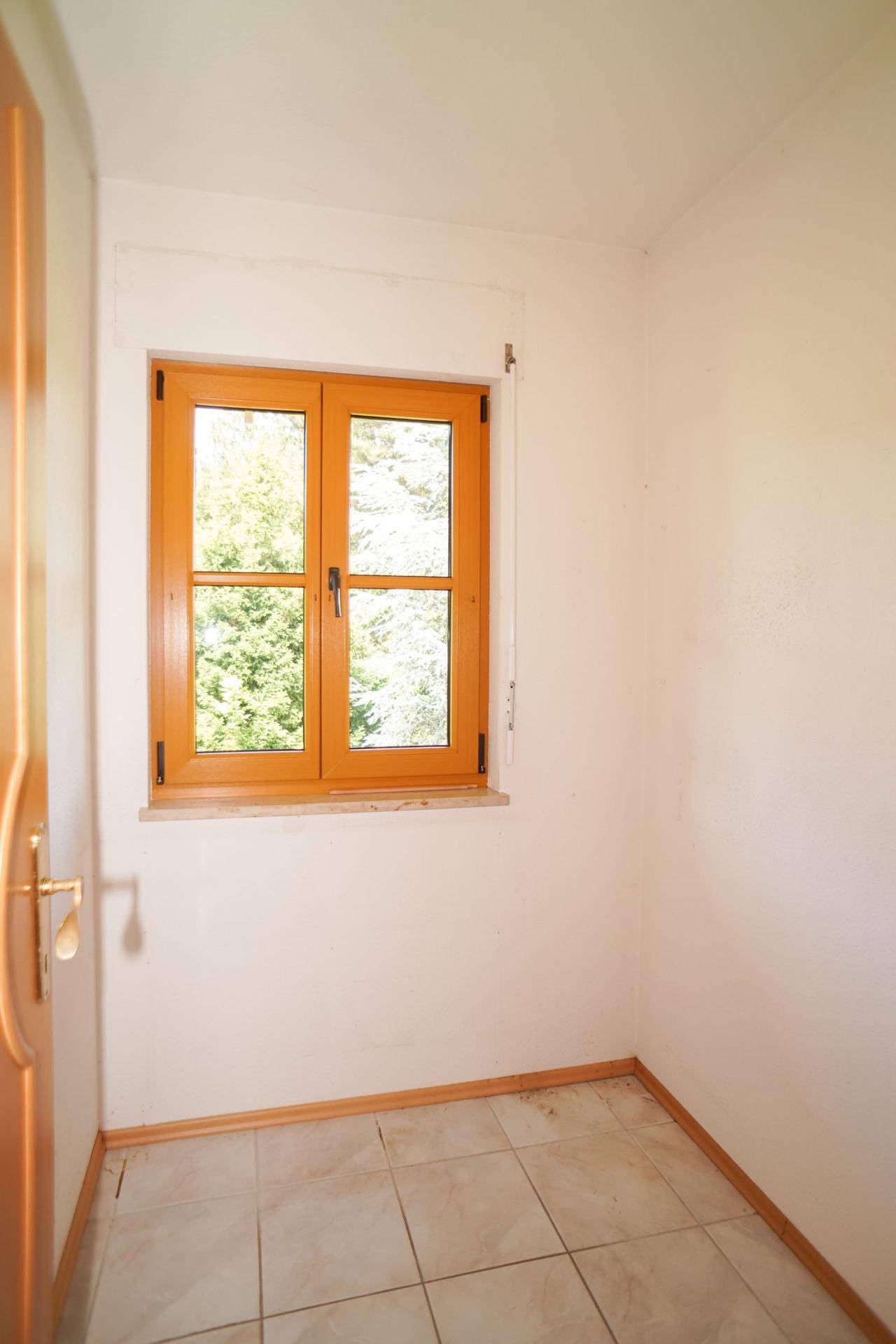 Kleiner Raum mit gefliestem Boden und einem Fenster, das viel Tageslicht hereinlässt.
